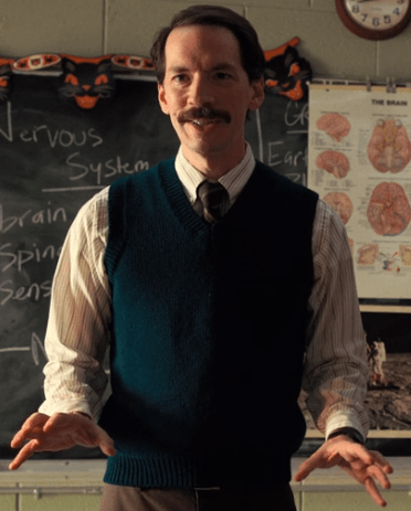 Debout devant un tableau noir rempli de formules, un jeune scientifique expose avec enthousiasme une démonstration scientifique à ses étudiants dans une salle de cour aux États-Unis. Scéal studio plateforme d'écriture créative.